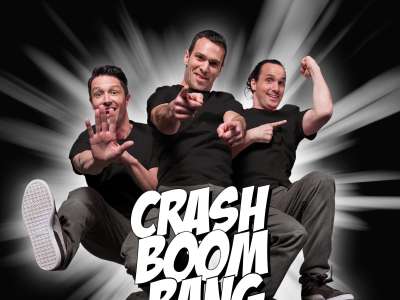 Drei Männer springen mit actiongeladenen Posen und Lächeln im Gesicht auf die Kamera zu. In weißer Schrift steht CRASH BOOM BANG. Das Bild ähnelt einem Bild aus einem Comic.