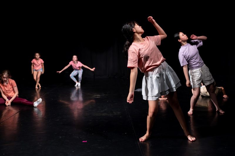 Kinder/Jugendliche in unterschiedlichen Positionen und Bewegungen in einem schwarzen Bühnenraum