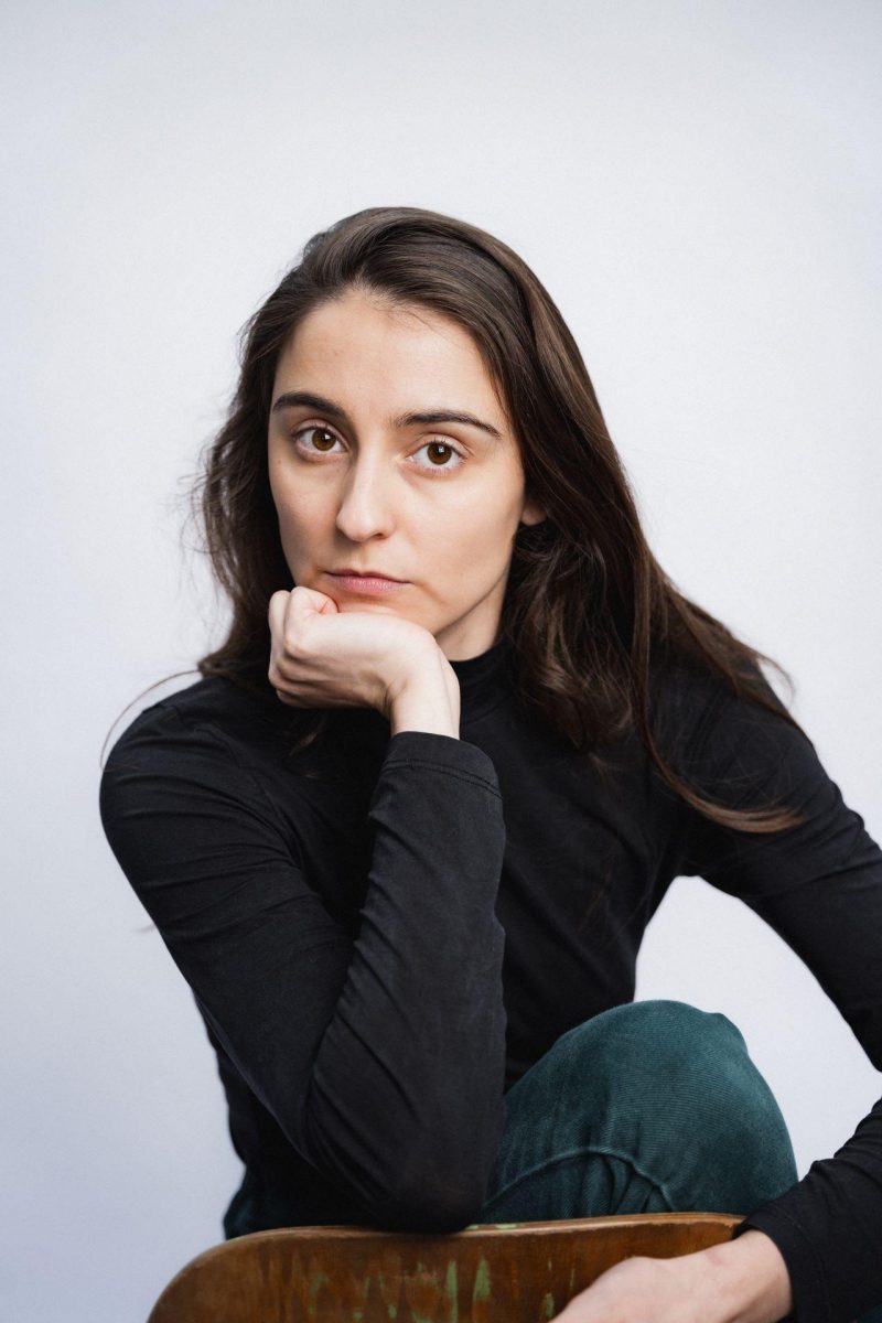 Anna Heithausen (eine junge Frau mit braunen Haaren und braunen Augen, trägt einen schwarzen Pullover) schaut in die Kamera. Dabei stützt sie den Kopf auf einem Arm ab.