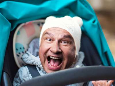 Ein Kinderwagen, in dem ein Kind mit dem Kopf von Lars Reichow sitzt (Bildmontage), der mit offenem Mund in die Kamera schaut.