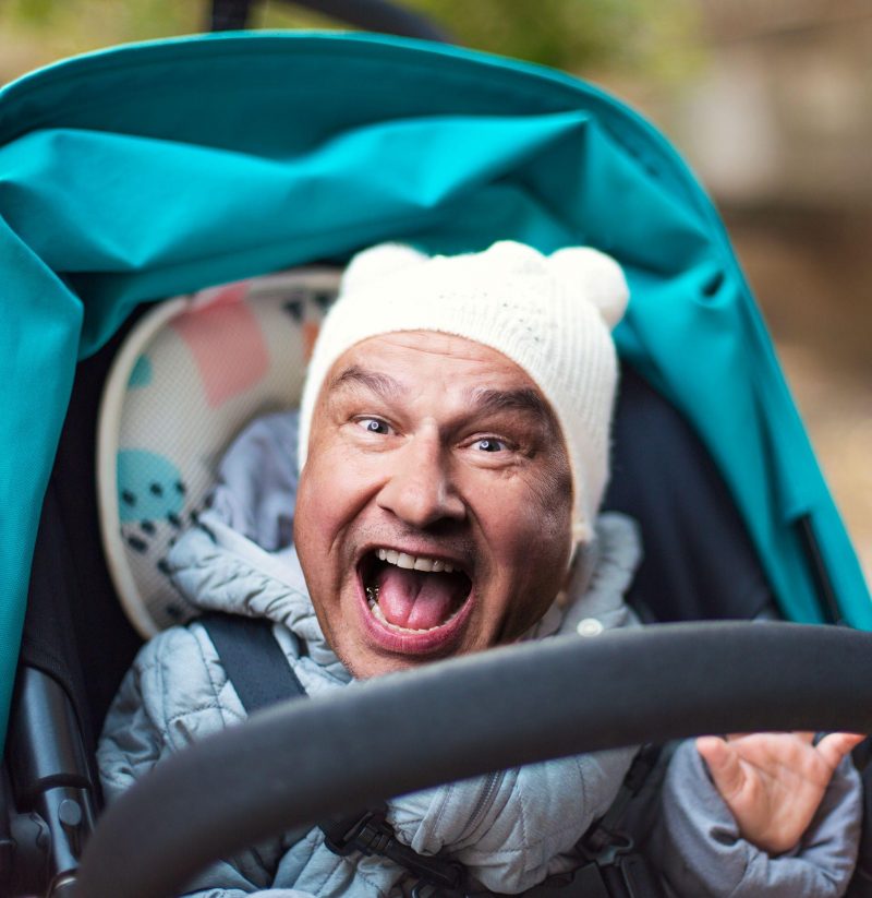 Ein Kinderwagen, in dem ein Kind mit dem Kopf von Lars Reichow sitzt (Bildmontage), der mit offenem Mund in die Kamera schaut.