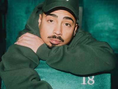 Tony Bauer (mit grünem Hoodie und grüner Baseballcap) lehnt sich nach vorne über einen Theatersitz, legt den Kopf auf seinen linken Arm, während der rechte Arm über die Rückenlehne des vorederen Sitzes baumelt.