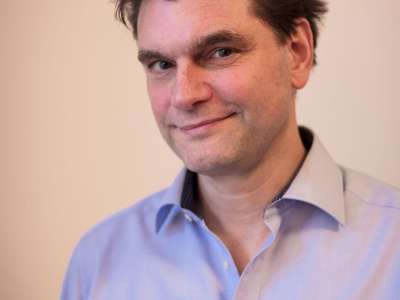 Lutz van der Horst (Mann mit dunklen, etwas struppig hochgegelten Haaren in einem hellblauen Hemd) blickt freundlich lächelnd in die Kamera.