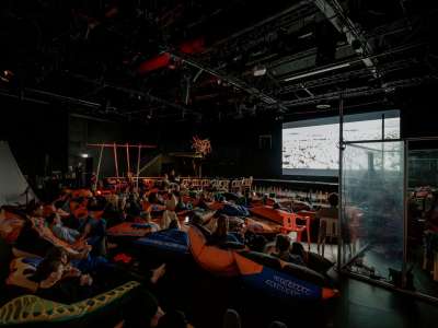 Menschen sitzen in Sitzsäcken und schauen einen Film, der auf eine Leinwand projiziert wird.